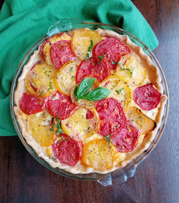 tomato pie topped with slices of yellow and red tomatoes and fresh basil