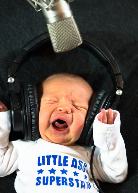 Newborn baby with headphones screaming into a microphone.