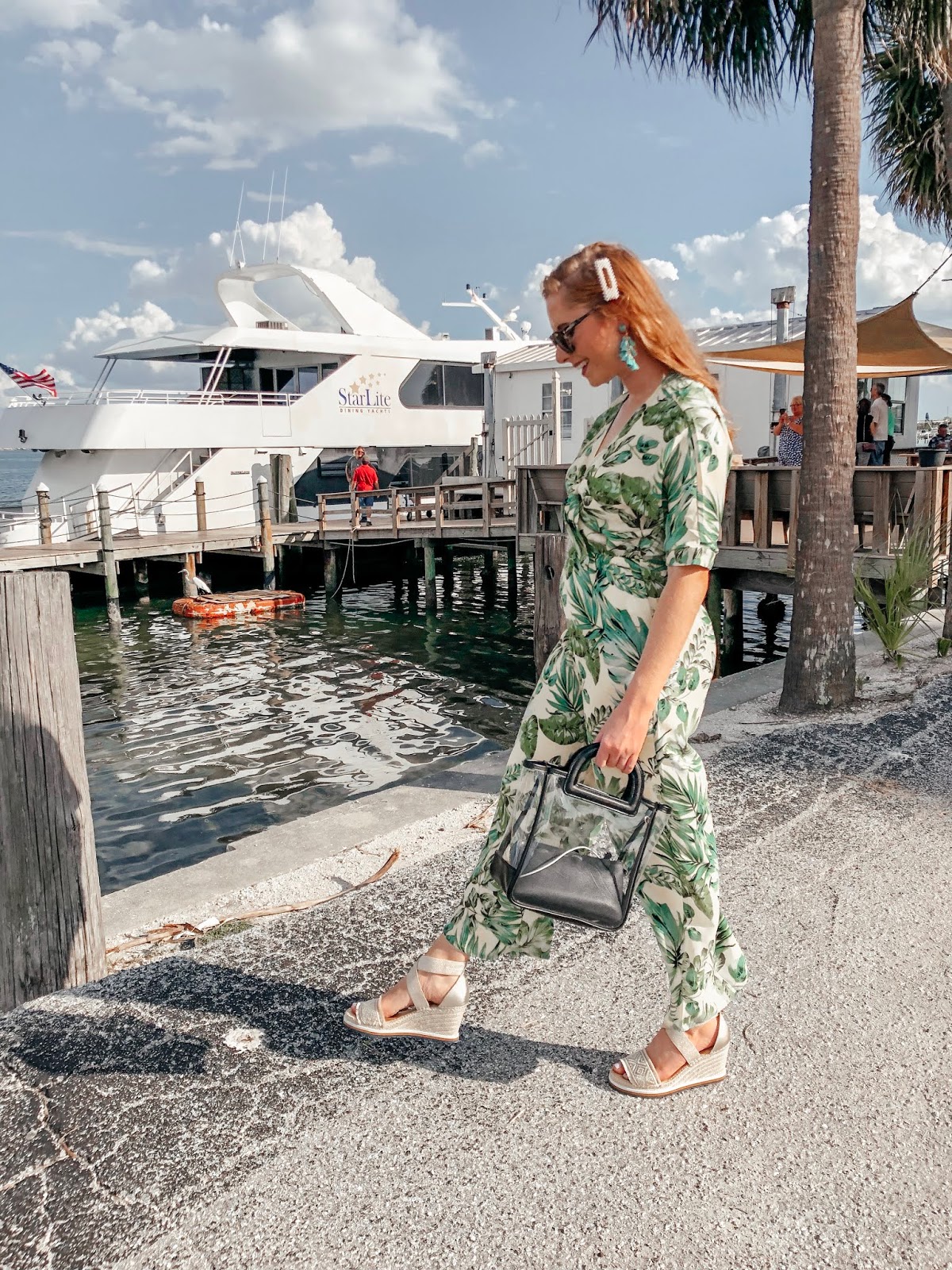 tampa blogger affordable by amanda wearing a yellow and green palm print jumpsuit from bealls outlet. she is walking in front of the starlite cruise ship. she is holding a clear bag from Target and wearing platform tommy hilfiger espadrilles from bealls outlet.
