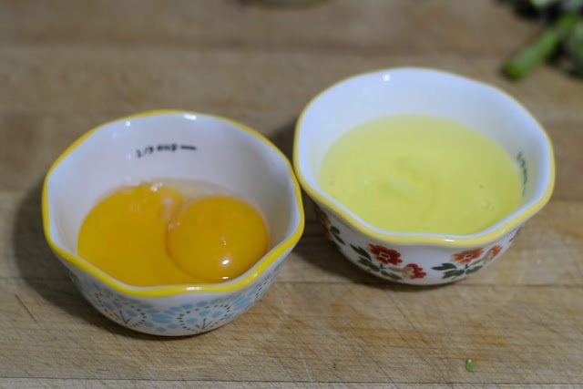 Two dishes on a cutting board.  One contains two egg yolks.  One containing the egg whites.