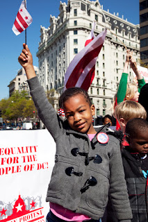 Six-year-old DC resident Lakaiela Dolmon waves the flag of DC from the stage in Freedom Plaza at a protest against federal taxation without representation and a rally for DC Statehood Friday, April 15, 2016. /Photo by Nancy Shia @nancy_shi