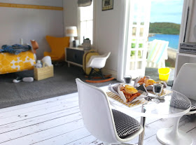 One-twelfth scale modern miniature motel room in white, grey and yellow overlooking the beach through open french doors.
