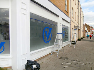 The Window Display window frosting with Vaparettes logo, a large 'V' with a circle around, in a bright blue has a frosted window behind it. Allowing light to pass through, a branding message and the stock room to be obscured by passing trade. The ladders are about to be climbed and the outside shop fascia is to be fitted above the window giving the building identity.