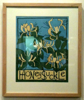 painting by Megan Moore of yellow honeysuckle blooms with a blue background and the plant name lettered in black across the bottom