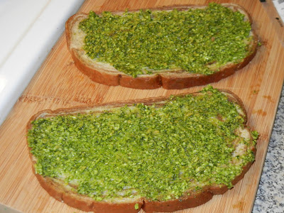 two pieces of pumpernickel bread with pesto on one side on a cutting board 