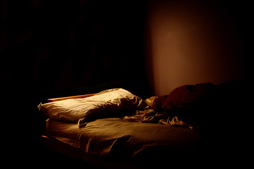 Imagen de una cama sola, de ambiente triste y a medio iluminar.