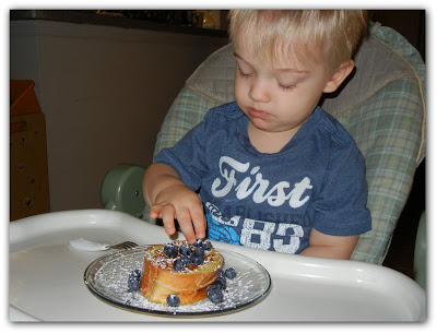 boy in a high char touching blueberry french toast that is on a plate 
