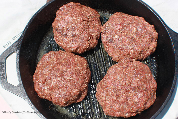 Raw hamburgers in a cast iron skillets with grids for making char marks on the hamburgers