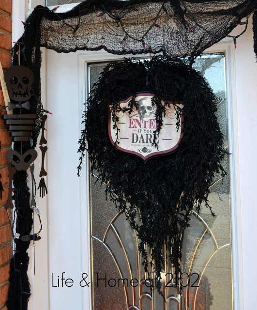 Front door decorated for Halloween with black wreath and skeleton.