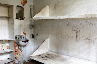 Prison cell with graffiti including cross on a white wall