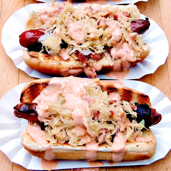 Reuben Hot Dogs in paper hot dog trays on a wooden background.