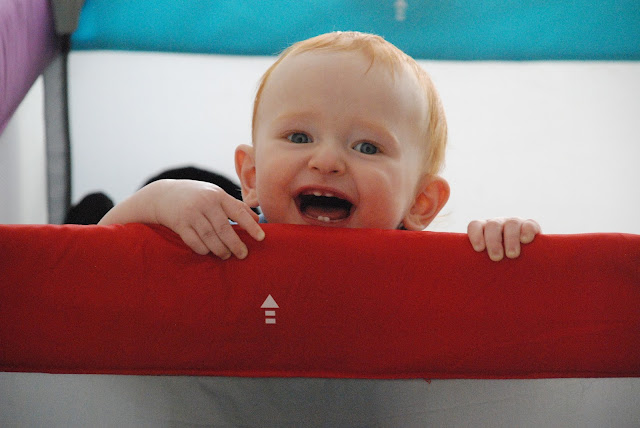 Redhead baby boy peeking over a travel cot