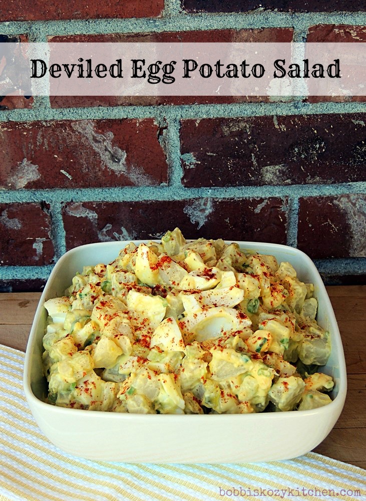 Deviled Egg Potato Salad in a white bowl in front of a brick wall.