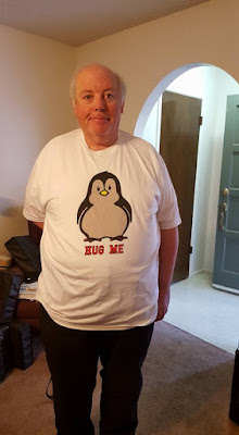 stands wearing a white T-shirt with a baby penguin image with the words hug me below the penguin.