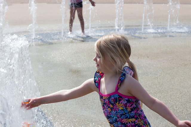 A girl in a swimming costume reaching it to a water fountain