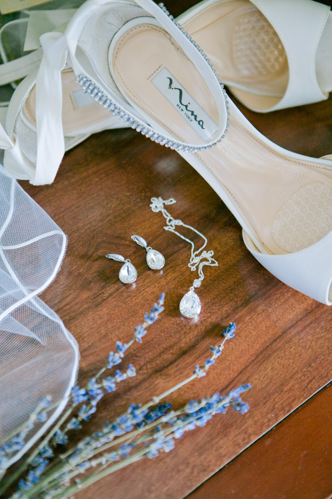 mina new york shoes lay next to a pair of fine diamond earrings and a delicate wedding veil