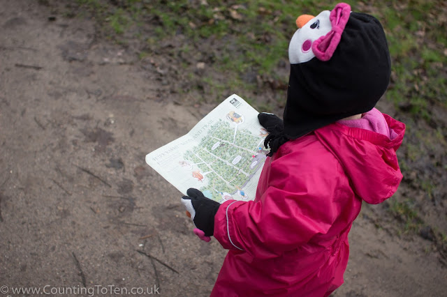 A toddler in a pink snow suit and penguin scarf and hat looking at a A4 map of the Peter Rabbit Trai at Langdon Nature Reservel