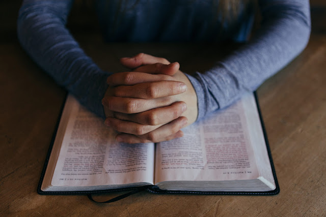 praying hands over book of Matthew in bible