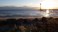 View from the shore of Brighton Jetty and beach with the sun setting on the horizon.