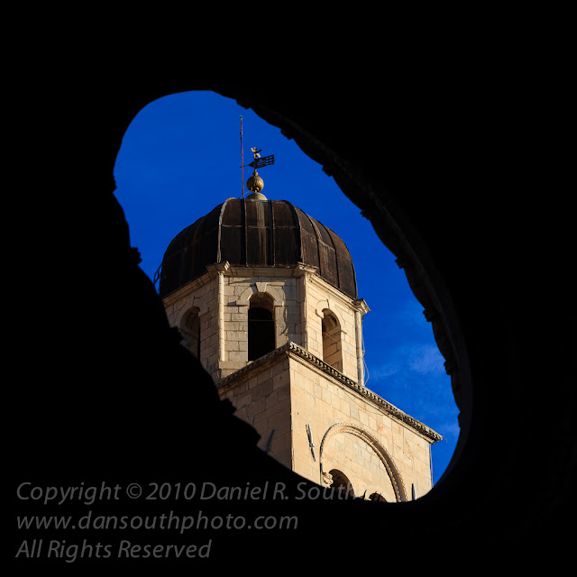 a fine art photograph of a church tower through a round window in dubrovnik, croatia