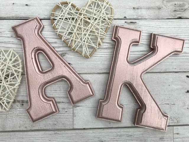 Wooden letters that have been spray painted rose gold next to some small wicker hearts