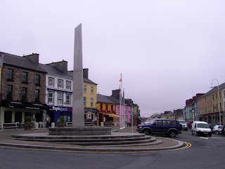 Obllisque statue in the middle of  a roundabout-cum-market-square in the middle of Clifden village, outside the Derryclare and EJ Kings pubs.