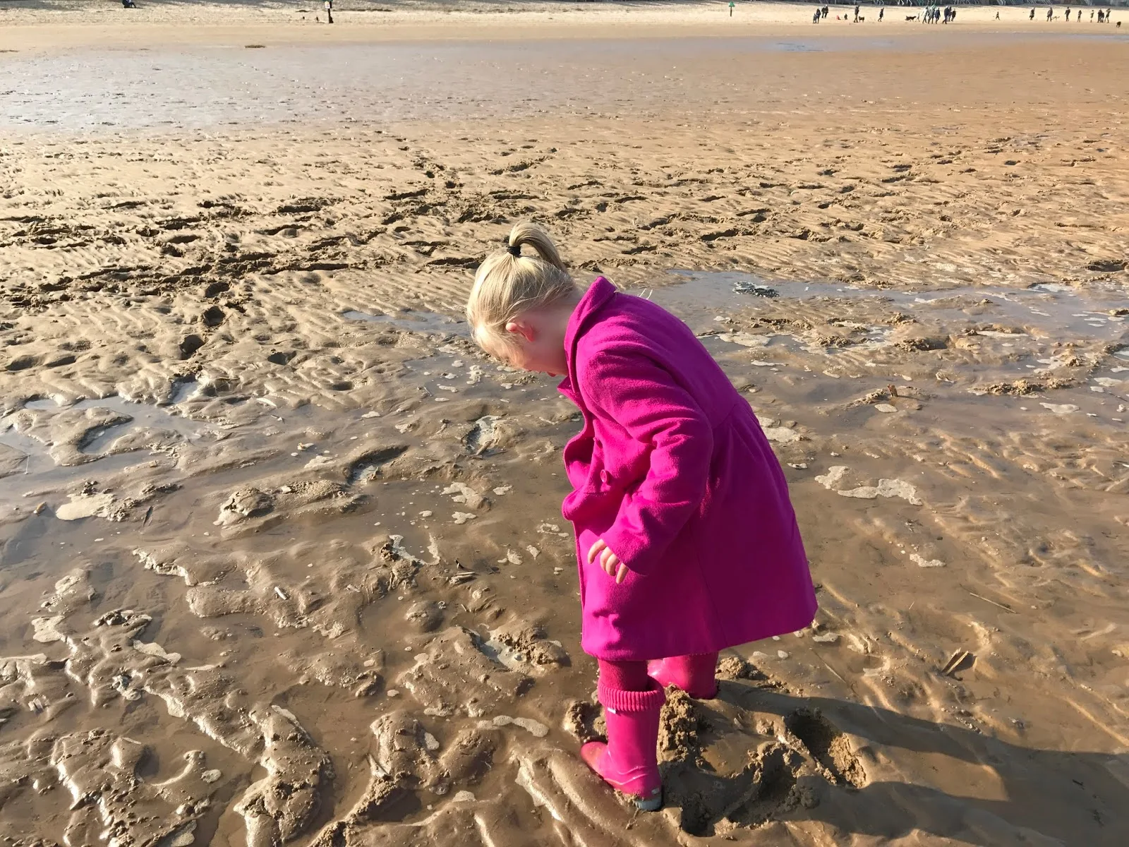 A 5 year old girl all dressed in pink looks down at her pink wellies as her feet sink in wet sand