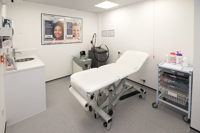 A white room with a massage bed, a few machines, a sink and a trolley