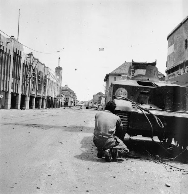 Tentara India Britania menembaki penembak runduk Indonesia di balik tank Indonesia yang terguling dalam pertempuran di Surabaya, November 1945.