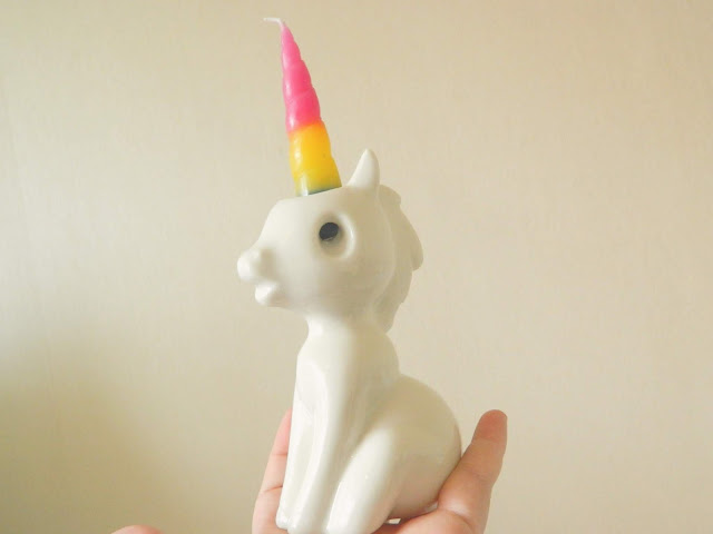 A white porcelian unicorn with a rainbow unicorn horn candle in it