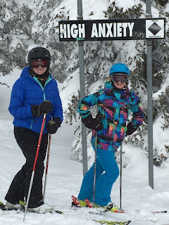 Snowy winter day with two ladies on skies posing below a black diamond ski sign call High Anxiety.