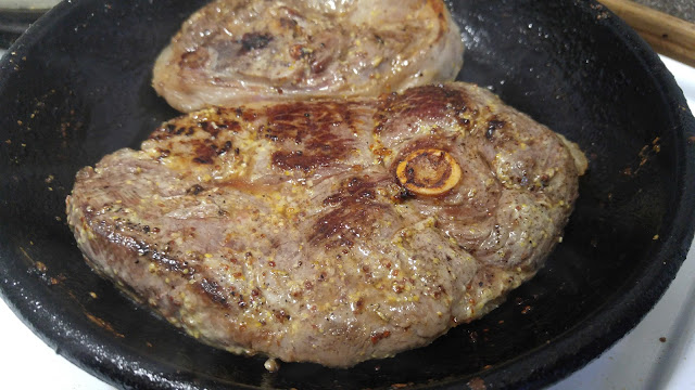 A lamb leg chop steak with a brown seared top in a black cast iron skillet. 