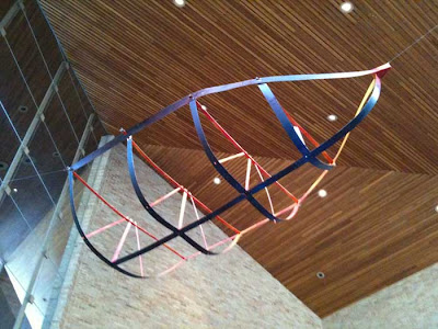 Metal straps joined together in the shape of skeletal boat, or a cage, suspended with wires from a ceiling