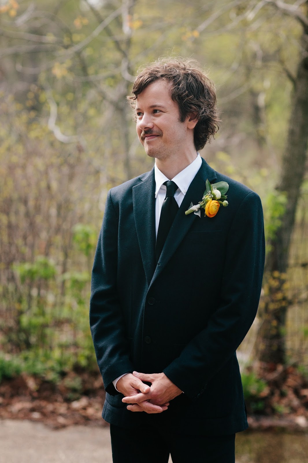 groom in a navy suit and black tie with a yellow ranunculus spring boutonniere