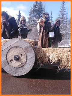Old wagon float with wooden wheels, guys in period furs, one with a helmet