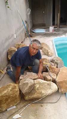 Bizzarri iniciando uma cascata de pedra na piscina com pedras ornamentais tipo pedra moledo na cor bege.