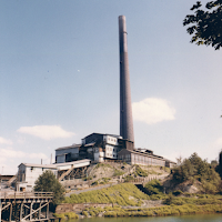 The smelter and stack are located on a hill. Water is in the foreground. 