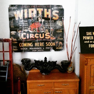 One-twelfth scale vintage circus poster on the wall of a miniature artist's studio, surrounded by various industrial-style pieces.