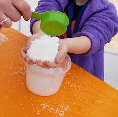 little hands full of play snow with water being poured in