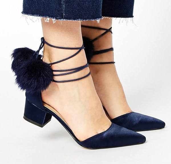 stock image of feet wearing ASOS blue satin shoes with fluffy pom pom ties on light background