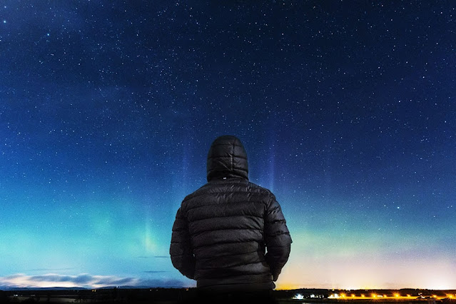 A man in a hooded coat looking at the northern lights