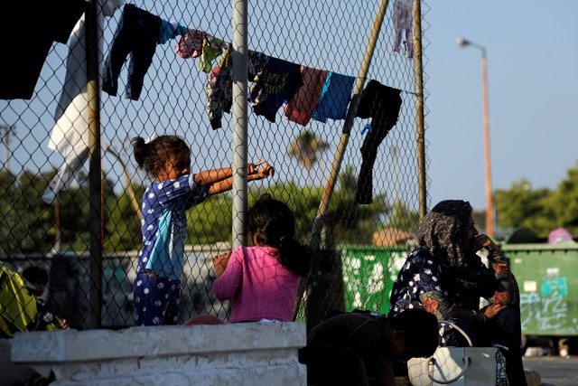 A woman sits by a wire fence with laundry hanging on it, while children play around her outside of disused Hellenikon airport, where stranded refugees and migrants are temporarily accommodated in Athens, Greece, August 10,  2016. REUTERS/Michalis Karagiannis