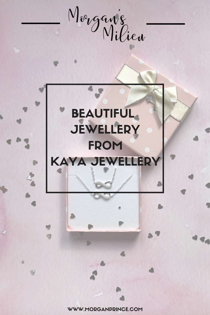 A silver infinity symbol necklace sits in its box atop a pink background. Over the top of the photo is a white translucent background with the words "Beautiful jewellery from Kaya Jewellery" surrounded by a black box. At the top of the picture is "Morgan's Milieu" logo. At the bottom of the page is "www.morganprince.com".