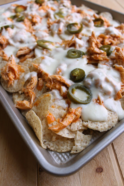 Crunchy tortilla chips topped with buffalo chicken, homemade cheese sauce and your favorite toppings. It's a perfect game day snack! sheet pan full of buffalo chicken nachos with white cheese sauce and jalapenos