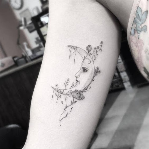 Uma personificação da lua crescente é adornado com flores, neste tatuagem prestados em que o portador da parte superior do braço.