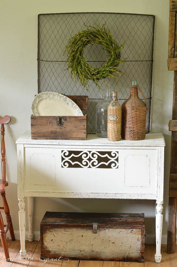 A wire mesh fireplace screen is used as a backdrop to a vignette and provides a perfect place to hang a boxwood wreath.