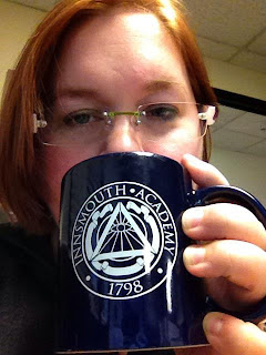 Author with auburn hair cut to the chin, wireless glasses, holding a dark blue-purple mug in front of her mouth.  Mug reads "Innsmouth Academy 1798" with a stylized Illuminati symbol