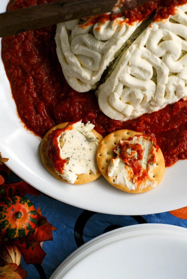 Two crackers with cheese ball spread on them on a white plate.