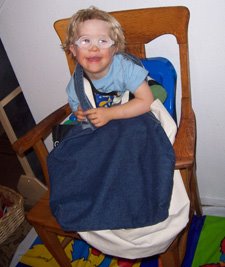 Lisa's young son sitting in a booster seat on a wooden chair, smiling, and wearing a blue shirt