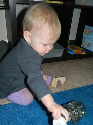 Young tot sitting on a blue rug and grabbing a bottle to "open and close"